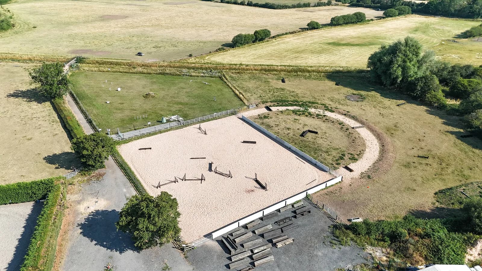 Aerial drone view of the outdoor sand arena and lunge pen at Trentvalley Equestrian Centre with show jumps set out